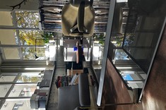 Strefa w showroomie Metaforma Design urządzona w loftowym stylu: nowoczesne fotele i szklany stolik kawowy odbijający światło wpadające przez duże okna. W tle ekspozytory prezentujące bogaty wybór próbek materiałów i tkanin dekoracyjnych